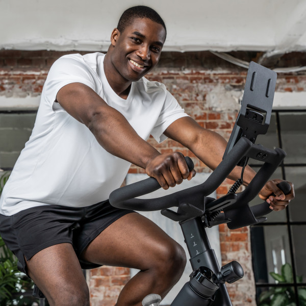 Nahaufnahme einer trainieren Person auf dem Kettler Indoor Cycle Speed 600 in wohnlicher Umgebung. Sie schaut lächelnd in die Kamera.